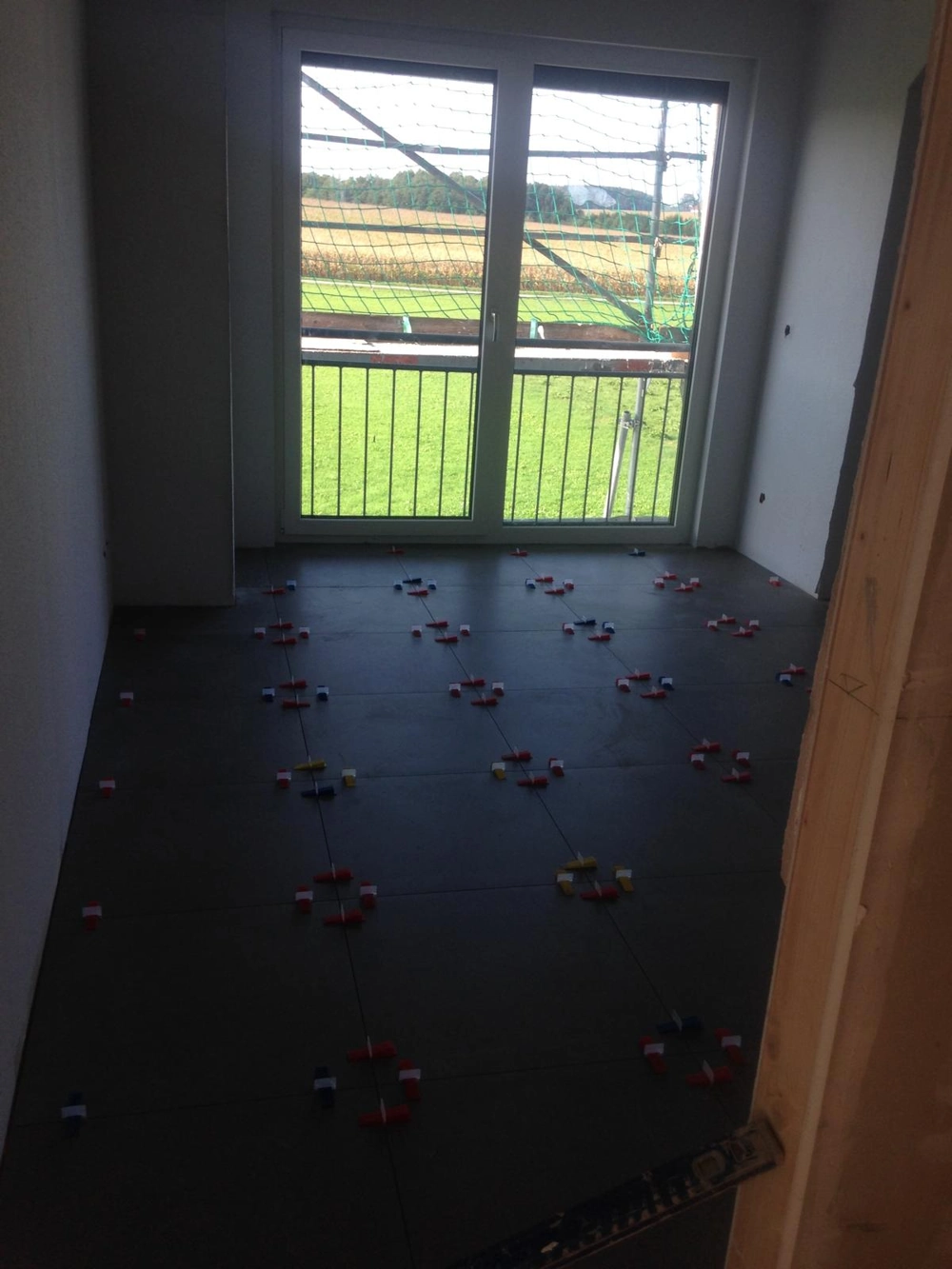 Bodenverlegung großer, dunkler Fliesen mit Abstandshaltern vor Balkonfenster, Fliesenarbeiten