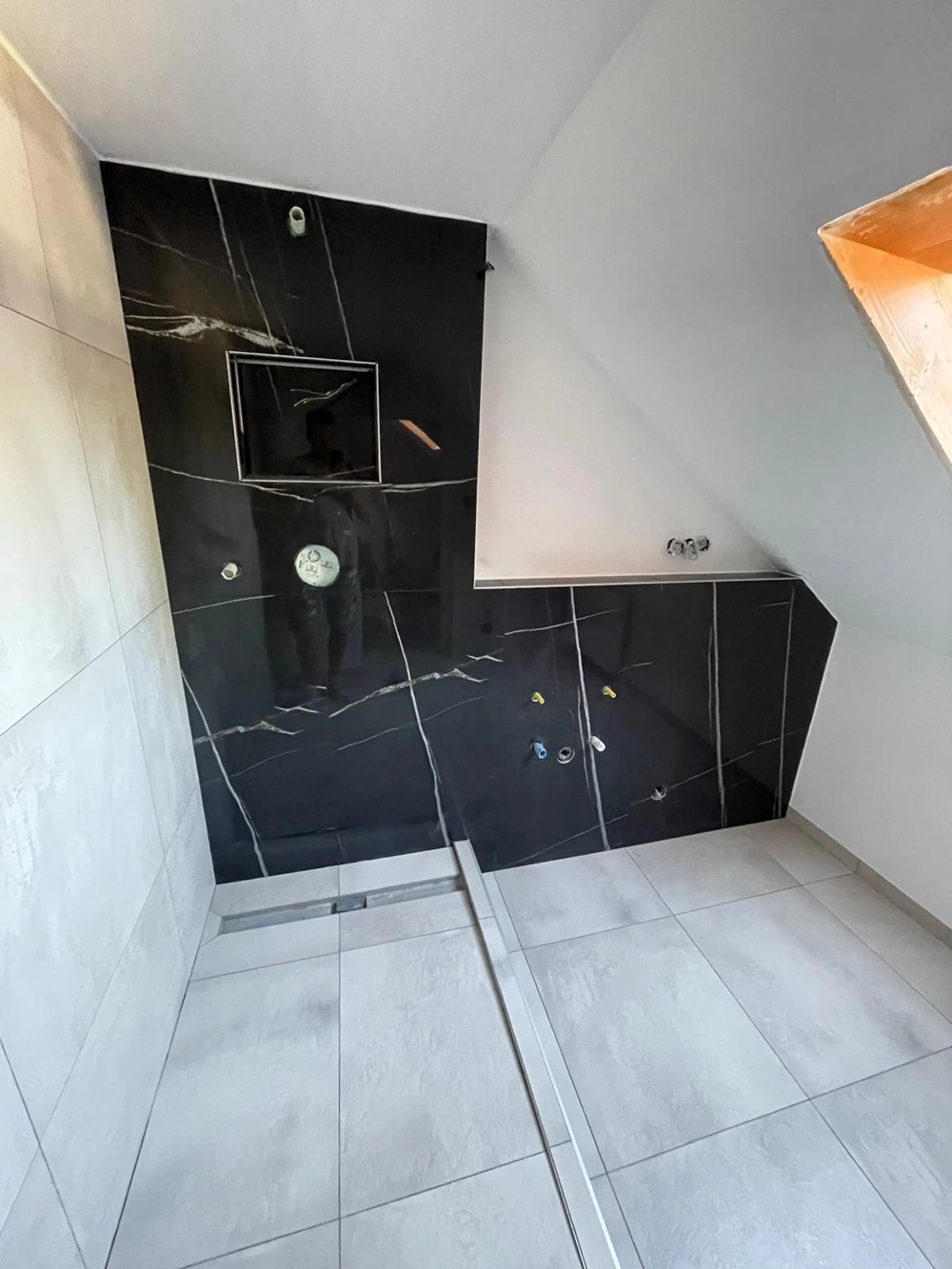 Fliesenarbeiten im Dachgeschoss: schwarz-marmorierte Wandfliesen, helle großformatige Bodenfliesen und integrierter Duschablauf