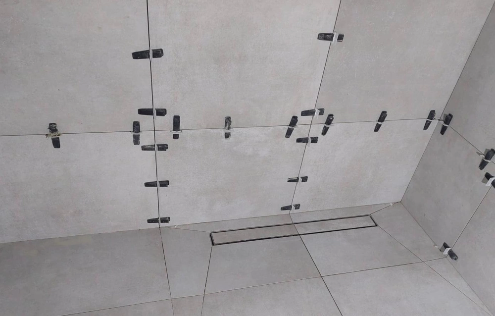 Graue großformatige Wand- und Bodenfliesen im Duschbereich mit Abstandshaltern – Fliesenarbeiten