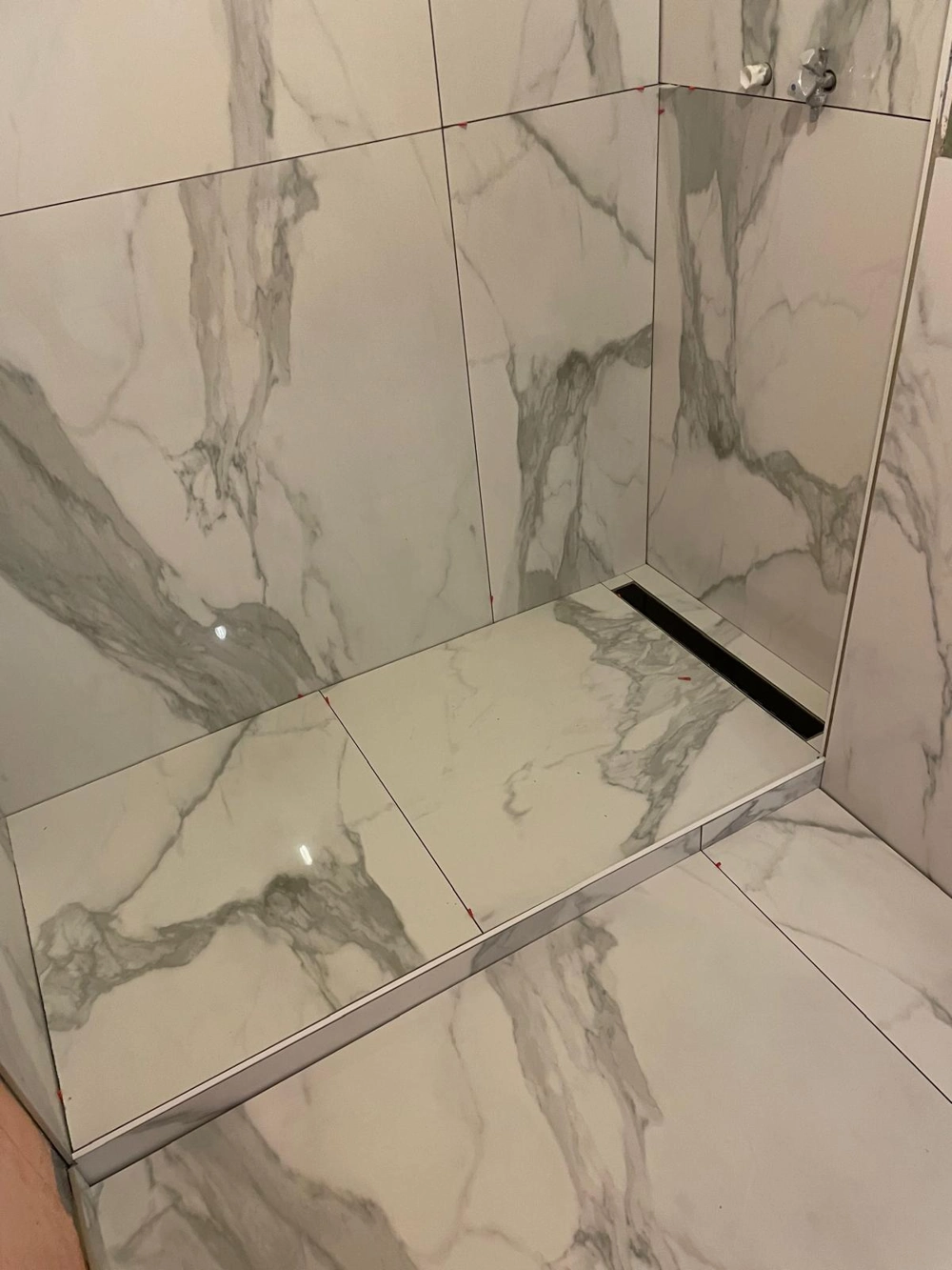 Frisch geflieste Duschnische mit weiß-grauem Marmor-Design und schwarzem Linienablauf - Fliesenarbeiten