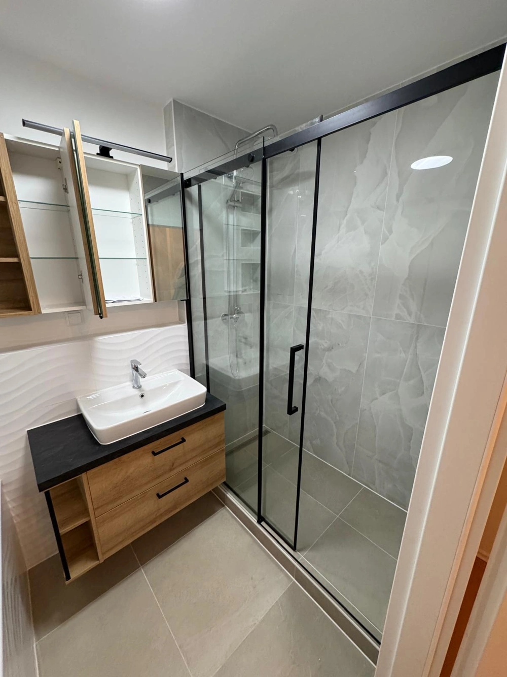 Moderne Duschkabinen aus Glas mit grauen Wand- und Bodenfliesen und hölzernem Badmöbel-Set