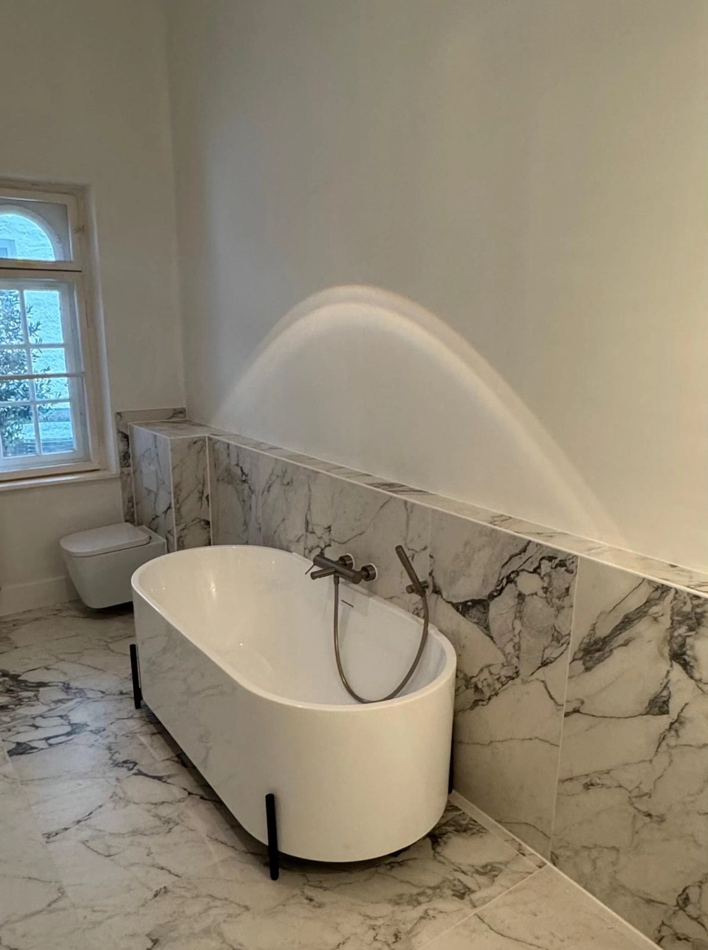 Freistehende Badewanne mit Wandarmatur vor Marmorfliesenwand – Sanitärinstallation
