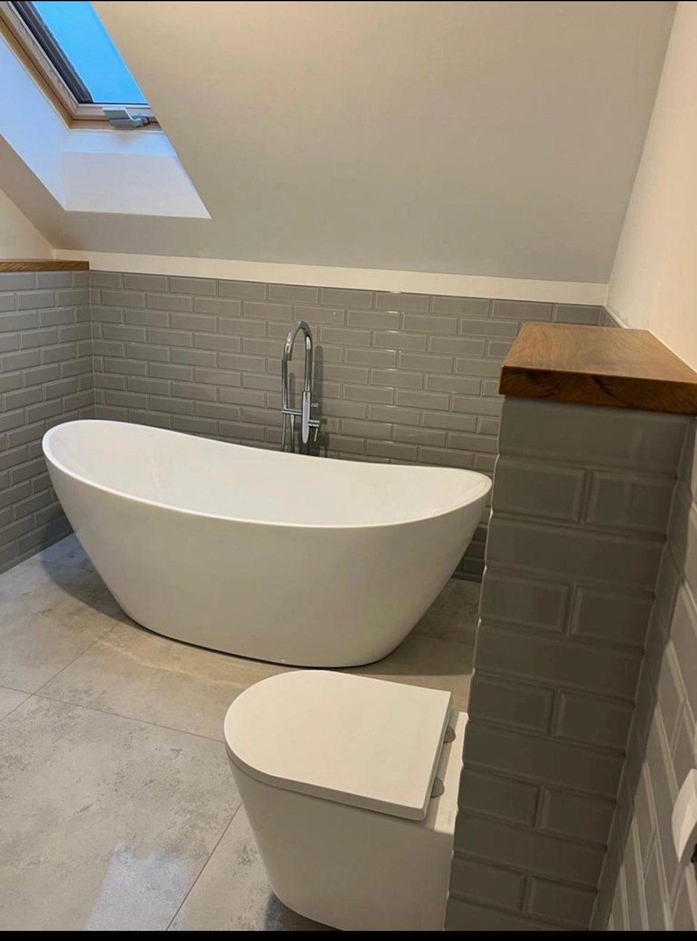 Modernes Badezimmer mit freistehender Badewanne, grauen Wandfliesen und Toiletteninstallation – Badezimmer Renovierung